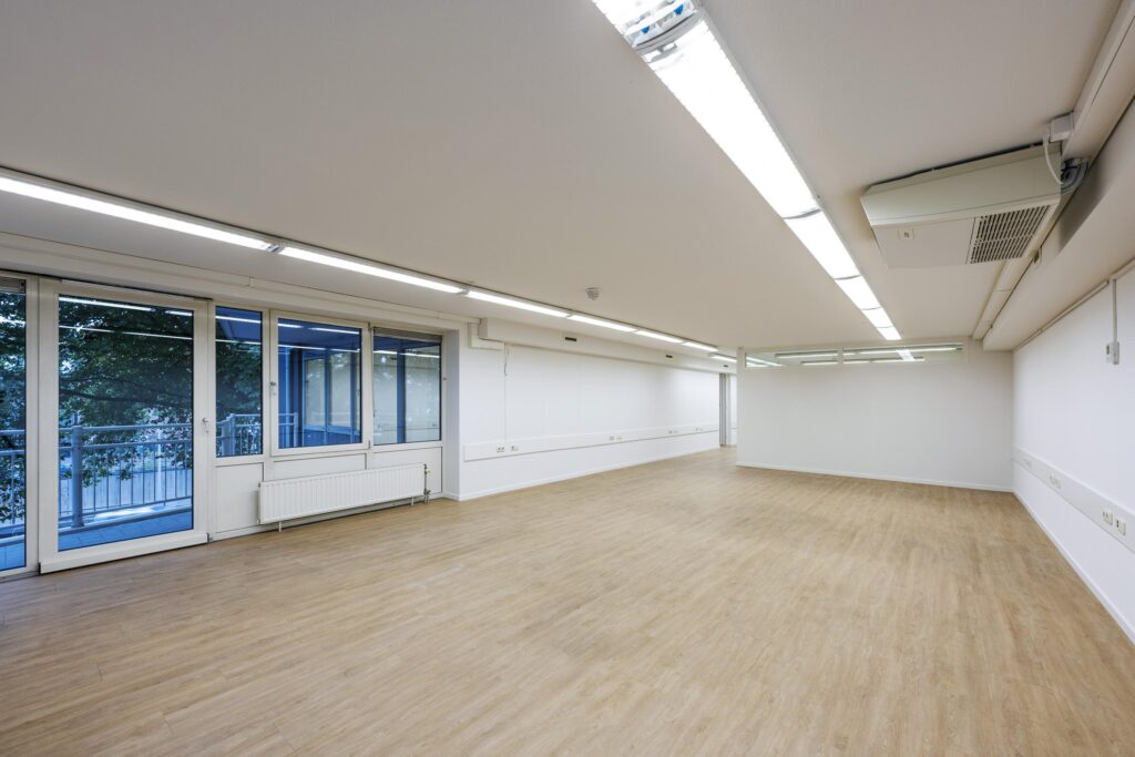 Lichte, lege kantoorruimte aan de Prins Hendrikkade met houten vloer, witte muren en grote ramen.